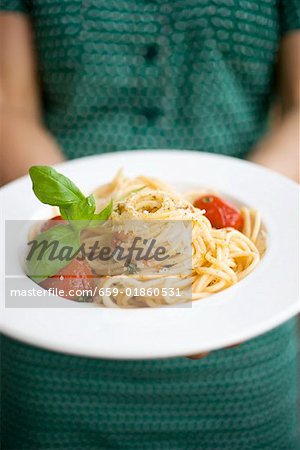 Woman holding plate of spaghetti with Parmesan and basil