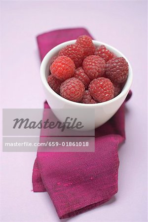 Raspberries in white bowl on purple cloth