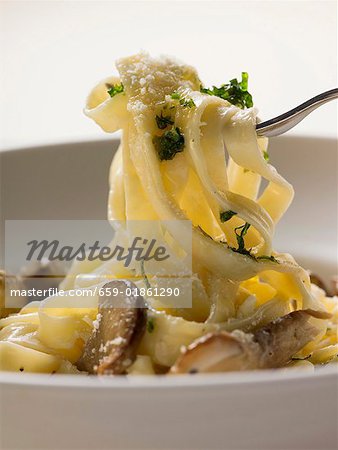 Tagliatelle with ceps and herbs on fork and plate
