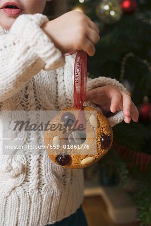 Child holding gingerbread tree ornament in front of Xmas tree