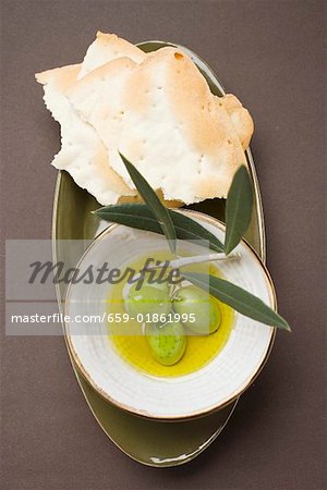 Olives vertes sur une brindille dans un bol d'huile d'olive, craquelins