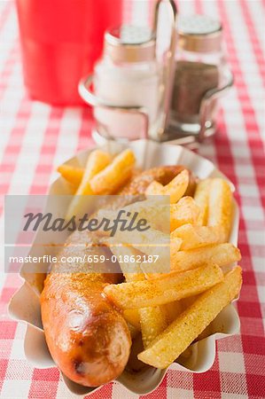 Sausage with ketchup & curry powder & chips in paper dish in restaurant