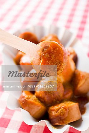 Sausage with ketchup & curry powder in paper dish, wooden fork