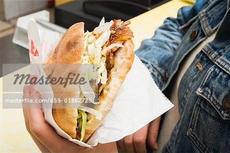 Mains tenant un döner kebab dans un snack-bar