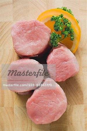 Four pork medallions, garnished with parsley and orange