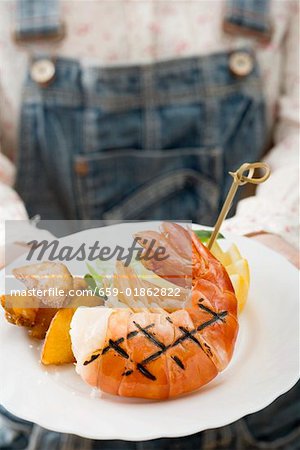 Person holding grilled king prawn on plate