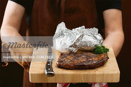 Homme tenant le steak de bœuf grillé sur planche à découper