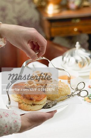 Mains servant des pâtisseries sucrées et scones pour manger avec du thé Mains servant des pâtisseries sucrées et scones pour manger avec du thé