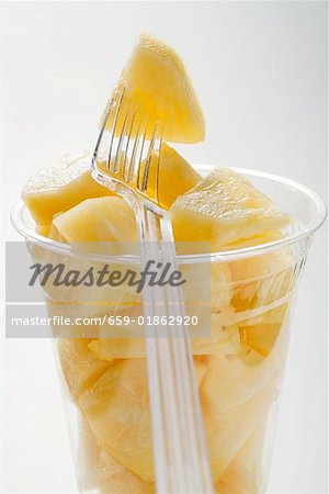 Pineapple chunks in a plastic beaker with a plastic fork