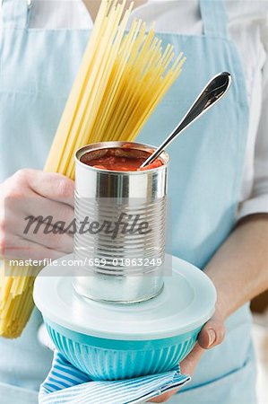 Femme tenant des spaghetti, pot de tomates & conteneur pour aliments