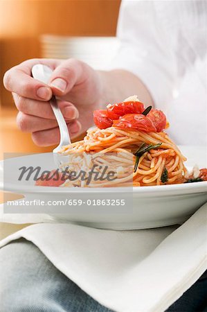 Person eating spaghetti with tomatoes and rosemary