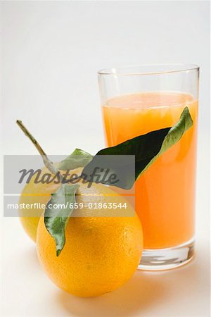 Verre de jus d'orange et de deux oranges avec des feuilles Verre de jus d'orange et de deux oranges avec des feuilles