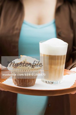 Femme tenant un plateau avec latte macchiato et muffin