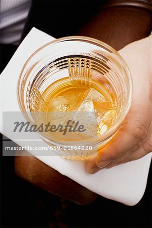 Hand holding glass of whisky with ice cubes Hand holding glass of whisky with ice cubes