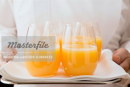 Femme de chambre au service de plusieurs verres de jus d'orange sur le plateau
