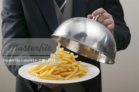 Butler lifting serving dome from plate of chips