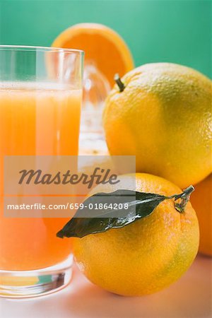 Glass of orange juice beside several oranges