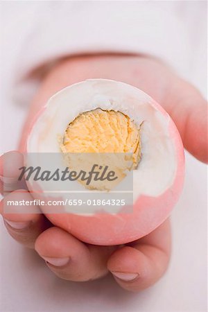 Child's hands holding coloured boiled egg with top cut off