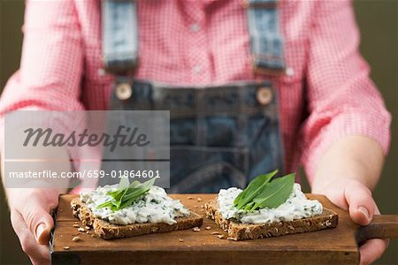Person holding wholemeal bread with quark & ramsons on board