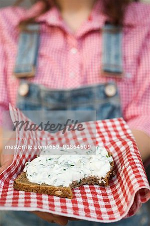 Woman holding wholemeal bread with quark & ramsons on napkin