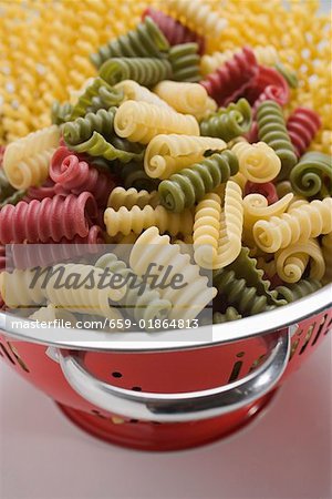 Coloured riccioli in colander, fusilli lunghi in background