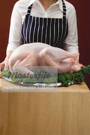 Woman holding platter with fresh turkey on parsley