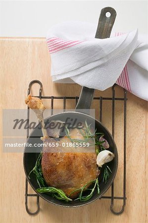Fried goose leg with rosemary in frying pan (overhead view)