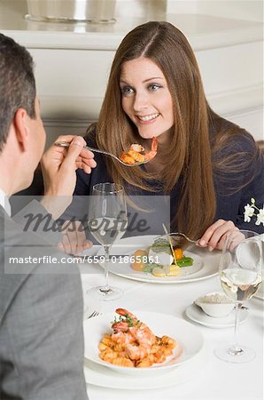 Man offering woman prawn on fork in restaurant