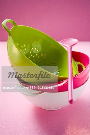 Coloured colanders, stacked, and pink cooking spoon