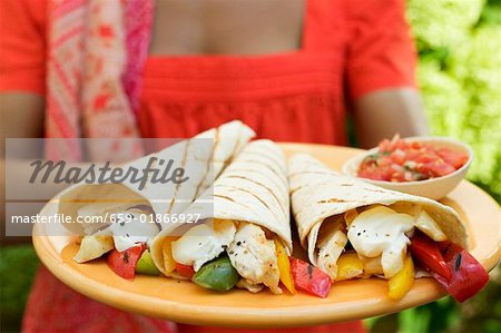 Woman holding plate of wraps and salsa