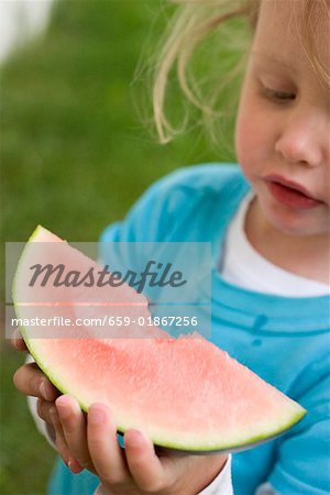 Petite fille tenant une tranche de melon d'eau avec une morsure prise