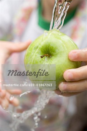 Child holding green apple under running water