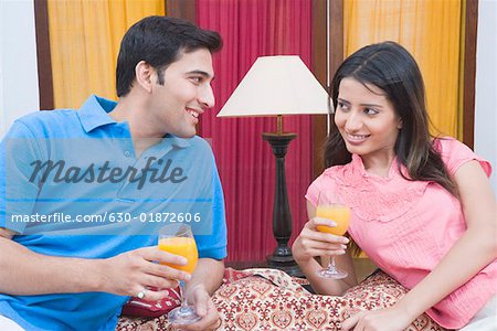 Jeune couple souriant et la tenue des verres de jus de fruits