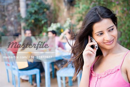 Gros plan d'une jeune femme parlant sur un téléphone mobile avec ses amis assis à une table à manger en arrière-plan