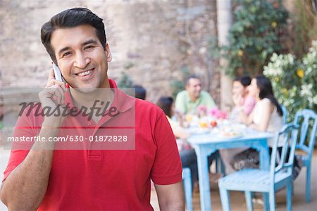 Portrait d'un homme adult moyen parler sur un téléphone mobile avec ses amis assis à une table à manger en arrière-plan