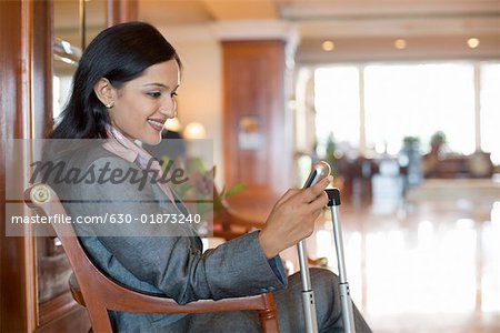 Side profile of a businesswoman text messaging on a mobile phone and smiling