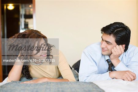 Businessman and a businesswoman lying on the bed and looking at each other