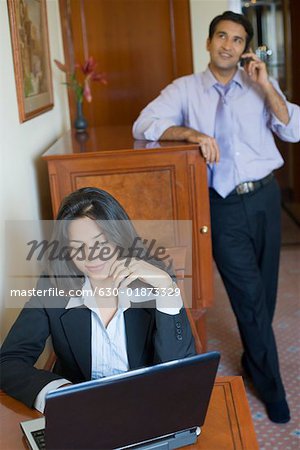 Geschäftsfrau arbeiten auf einem Laptop mit einem Geschäftsmann auf einem Mobiltelefon im Hintergrund sprechen