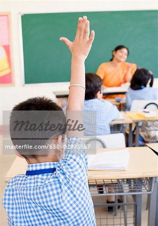 Vue arrière d'un écolier dans une salle de classe avec sa main levée