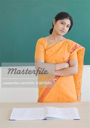 Portrait of a female teacher standing in front of a blackboard with her arms crossed