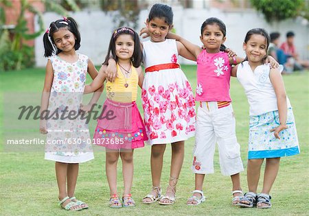 Portrait of five girls standing together in a lawn and smiling