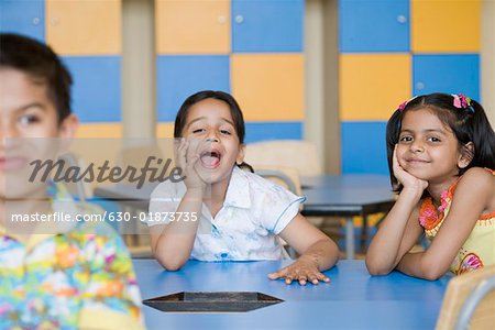Portrait of a schoolgirl sitting with her friends in a class room and shouting