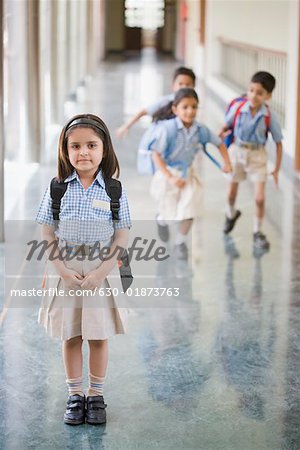 Portrait of a schoolgirl standing in the corridor with three student running in the background