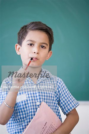 Portrait d'un écolier tenant un crayon et un livre devant un tableau noir