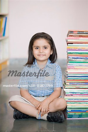 Portrait d'une collégienne assis sur le sol avec une pile de livres