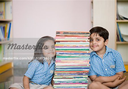 School boy and a schoolgirl sitting on the floor with a stack of books