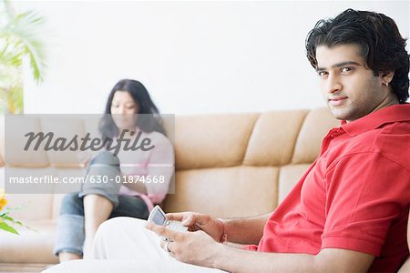 Seitenansicht eines jungen Mannes, der ein Mobiltelefon mit einer jungen Frau, die neben ihm sitzen halten
