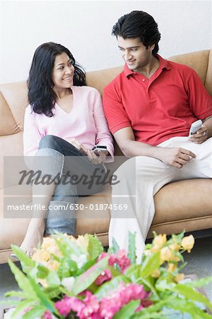 Young couple sitting with mobile phones on a couch and smiling