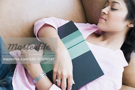 High angle view of a young woman sleeping on a couch with a book