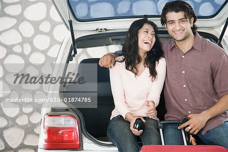 Young couple sitting on the boot of a car and smiling